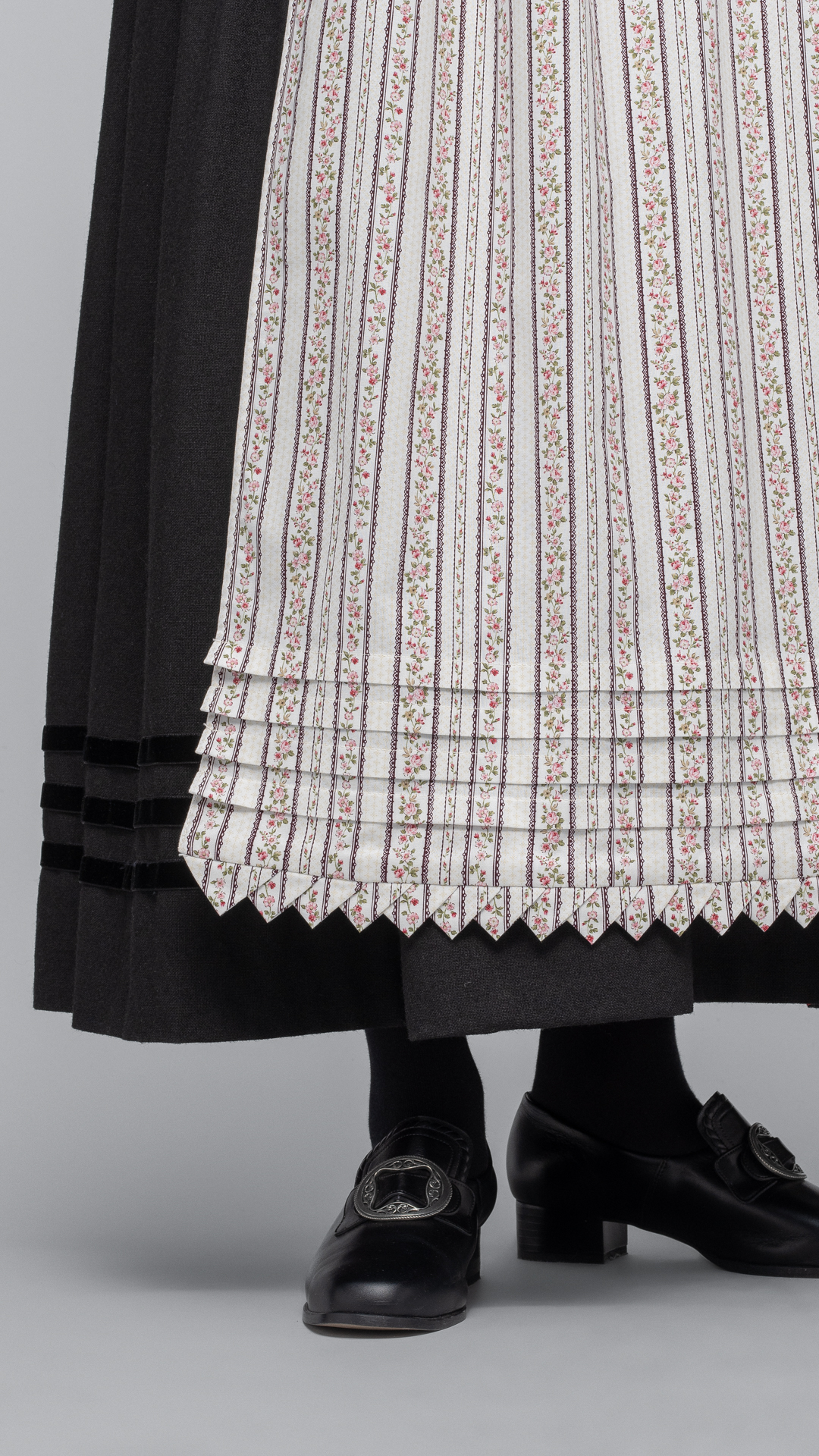 <span style="font-size: 19.2px; line-height: 27.648px;">Man kan bruke flere typer forkle til Fanabunaden. Kulørt forkle var mye brukt store deler av 1800-tallet og i høyeste høytid brukte man det hvite forkleet med heklekanter. Kulørt forkle er et bomullsforkle med blomstertrykk. Bunnen er lys og mønsteret kan variere. </span>‘ /><img data-image-id=