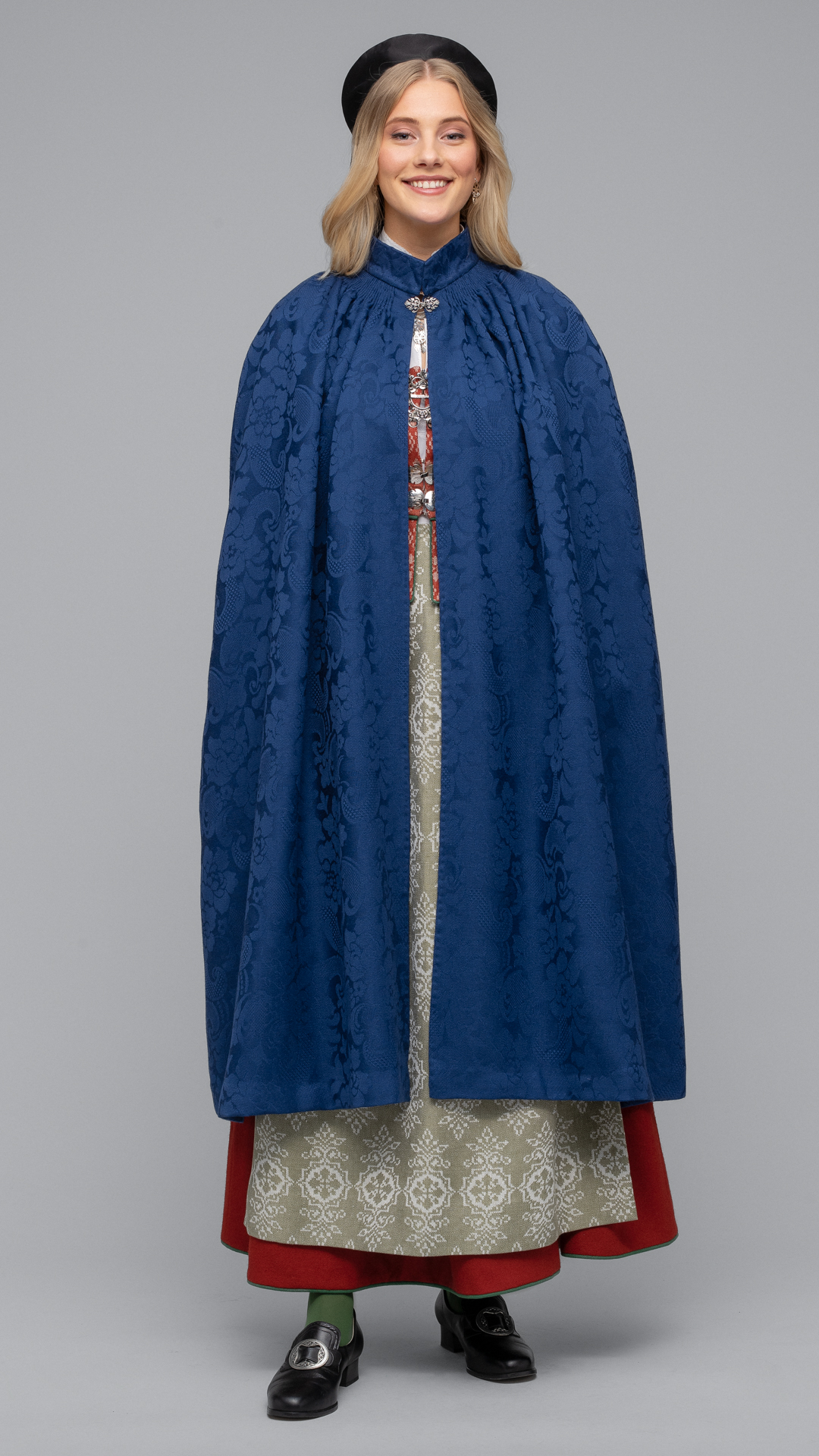 <p>Capen finnes i blå ulldamask med svart for. Lengden skal være ca. 40 cm over gulvet. Ytterplagget til Trønderbunaden er basert på fem gamle caper som ble funnet på Trøndelag Folkemuseum og i Trøndelags tekstilsamlinger.</p>‘ /><img data-image-id=