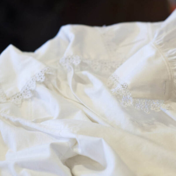 Er handlaga i kvitt bomullsstoff. Langs kragen er der oftast nupereller